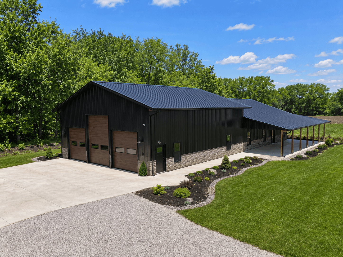 Aerial view of a finished commercial pole barn with black metal siding, stone wainscoting, and wood-grain garage doors