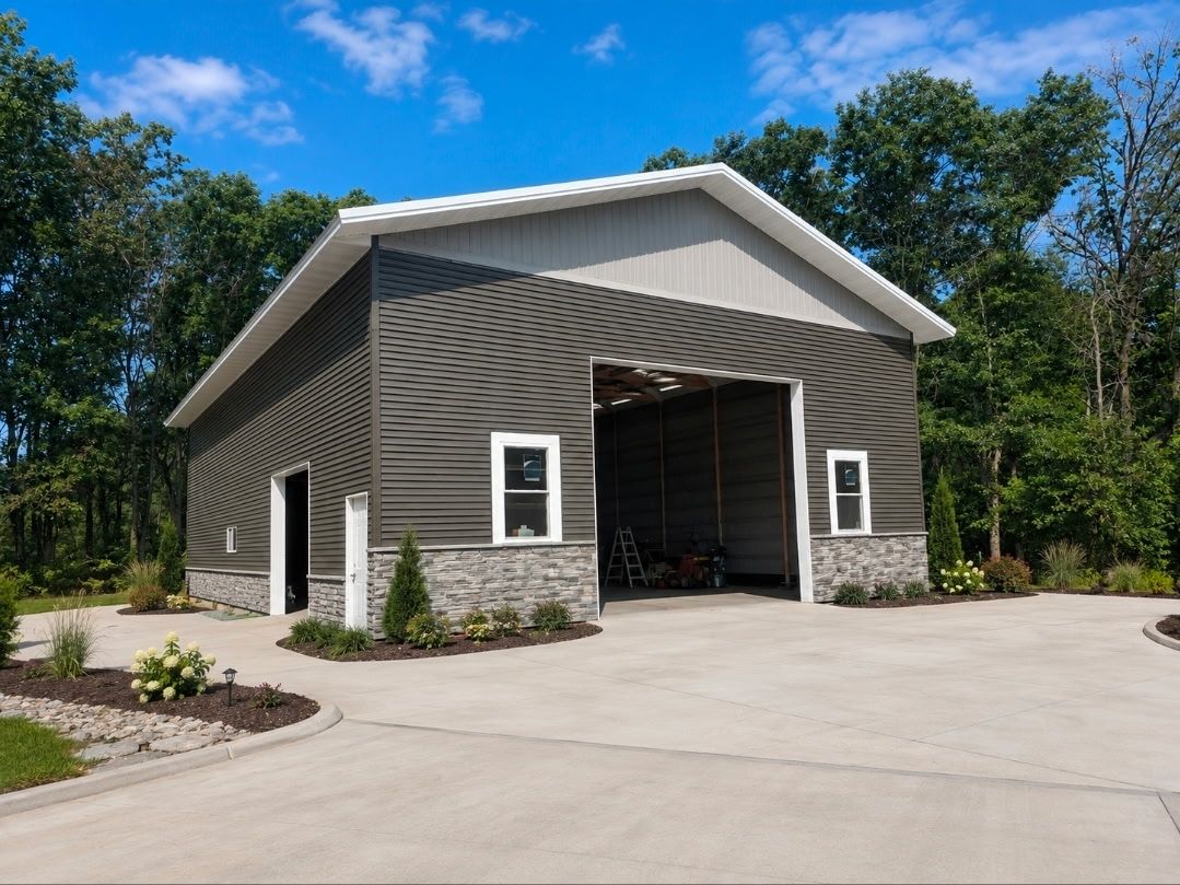 Large gray metal shop building with white trim, open bay doors, and covered porch