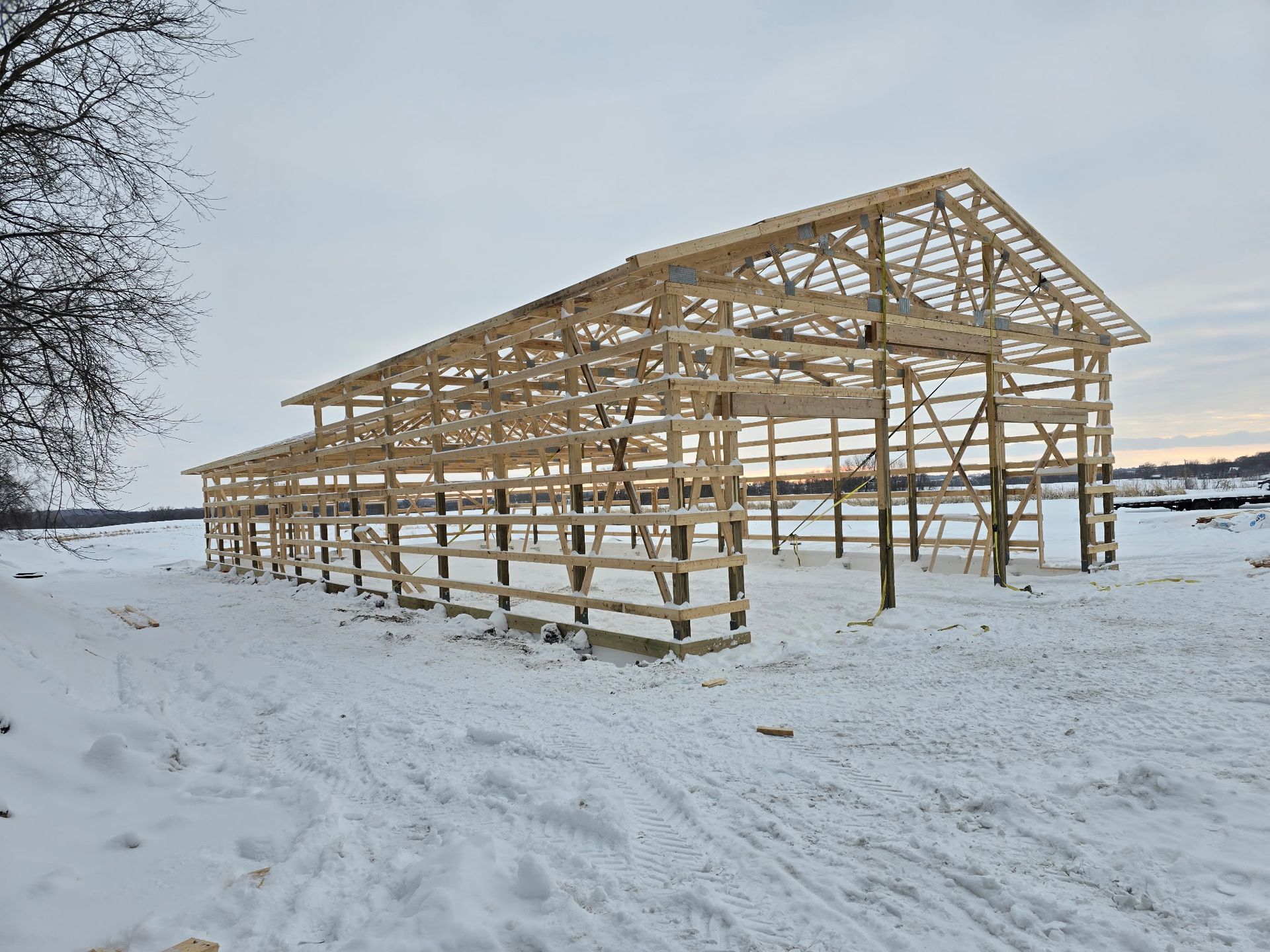 Roof framing progress on a snowy pole barn site